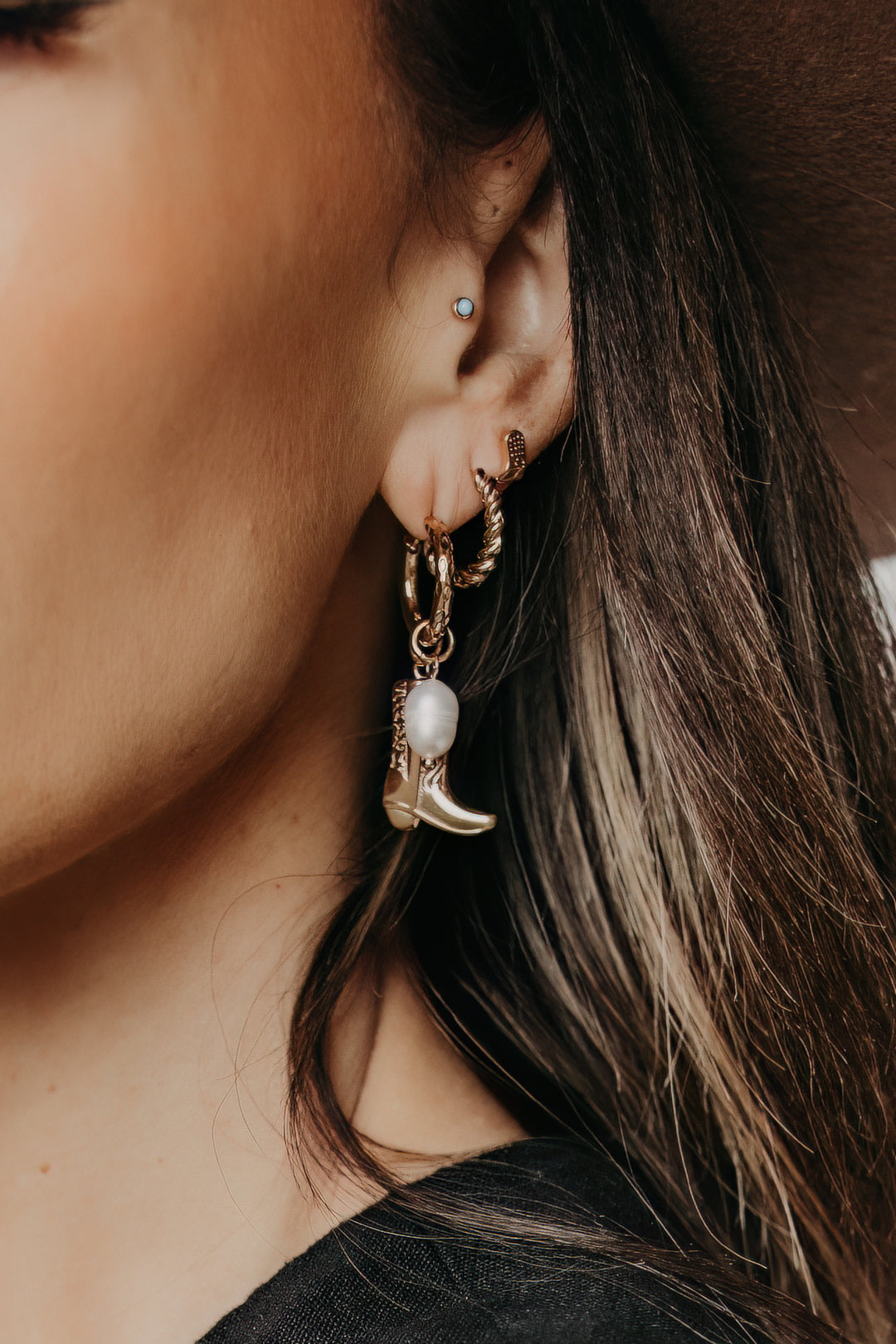 Close-up of a person wearing gold hoop earrings with a cowgirl boot design.