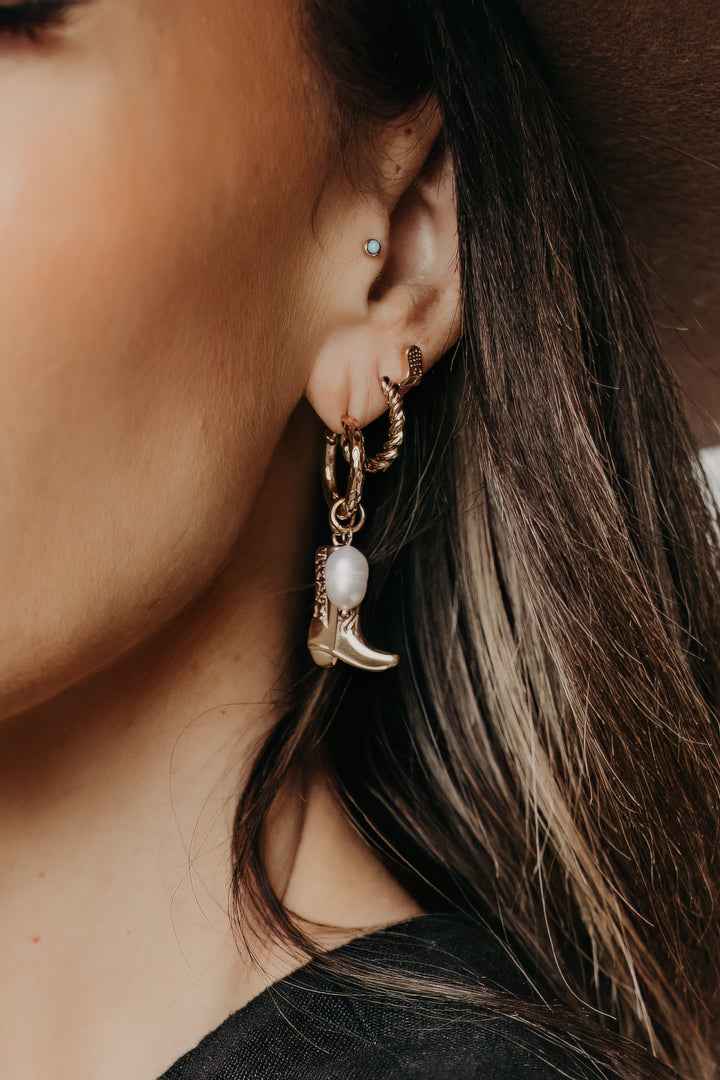 Close-up of a person wearing gold hoop earrings with a cowgirl boot design.